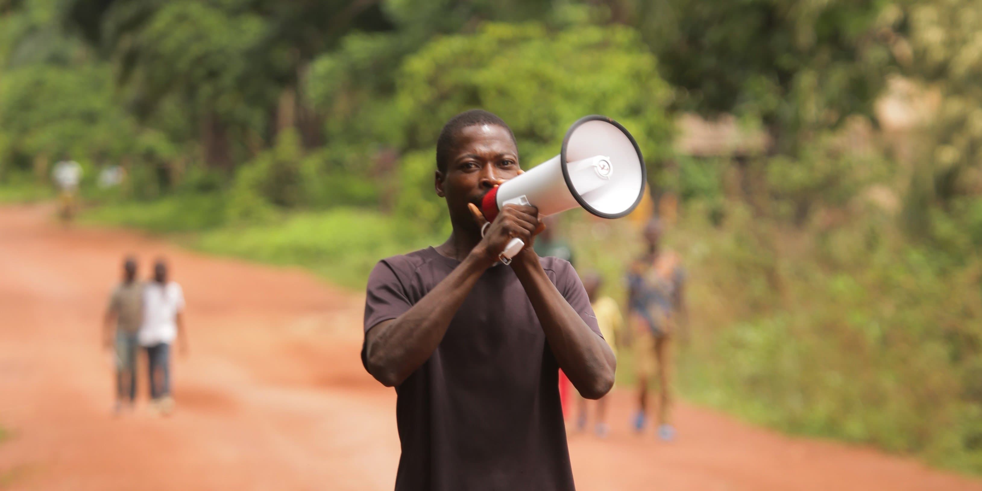 A young man holds a megaphone as he raises awareness about the yellow fever vaccination campaign in the DRC.